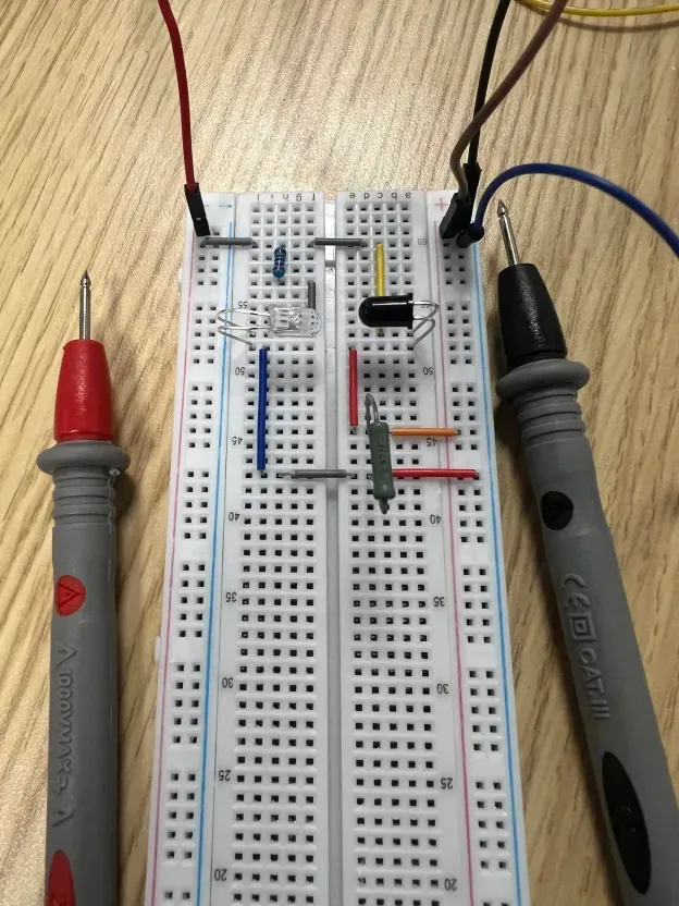 Multimeter probing the IR LED and phototransistor setup on a breadboard